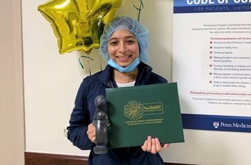 Abheena Jacob holds a Daisy Award and certificate in front of balloons in a Pennsylvania Hospital hallway.
